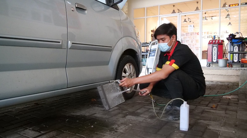 Teknisi membersihkan evaporator AC mobil secara berkala untuk perawatan 
