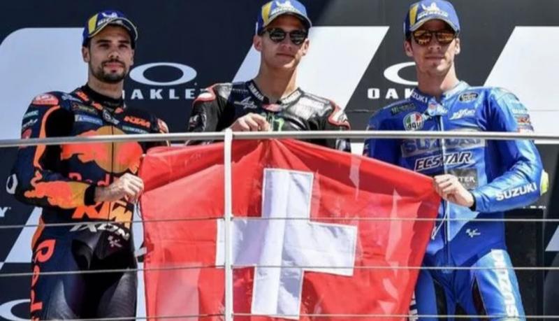 Fabio Quartararo memegang bendera Swiss di podium MotoGP Mugello Italia sebagai tanda duka mendalam atas meninggalnya pembalap Moto3 Jason Dupasquier. (Foto: crash)