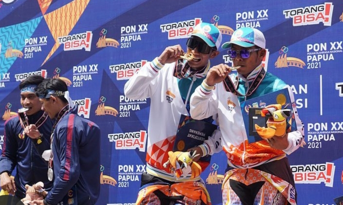 Boy Arby Febri dan Gupita Kresna (Papua) dengan ekspresi bahagia menggigit medali emas yang diraihnya di kelas Modifikasi Beregu balap motor PON XX Papua